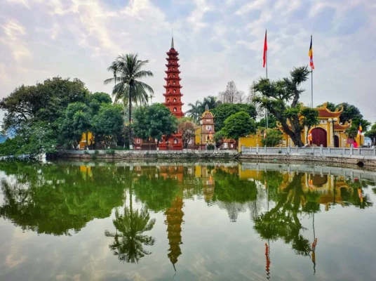 Chùa Trấn Quốc Hà Nội bên Hồ Tây với tháp đỏ nhiều tầng, cây xanh và mặt hồ phản chiếu cảnh chùa.
